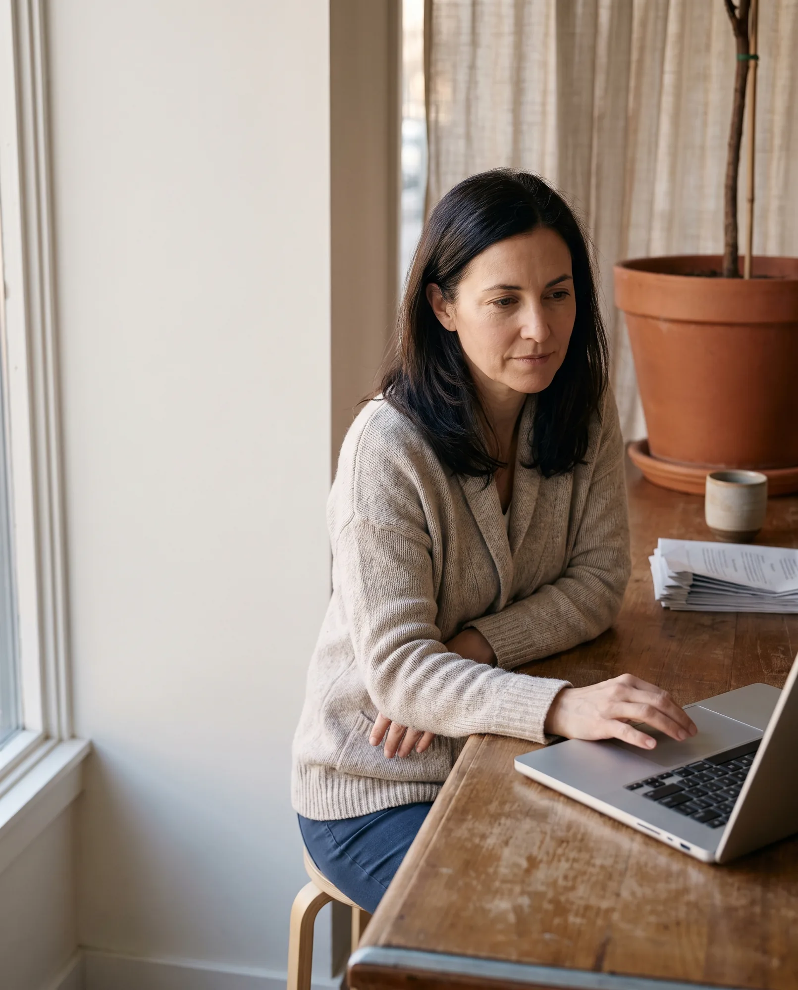 Owner of a small holistic practice reviewing her laptop at a sunlit wooden desk